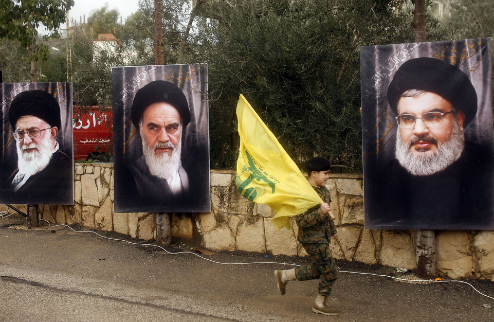 A boy carried a Hezbollah flag in Jibchit, Lebanon, in February as he ran past portraits of, from left, Ayatollah Ali Khamenei, the current supreme leader of Iran; Ayatollah Ruhollah Khomenei, the leader of Iran's Islamic Revolution; and Hassan Nasrallah, the leader of Hezbollah. Mahmoud Zayyat/Agence France-Presse — Getty Images