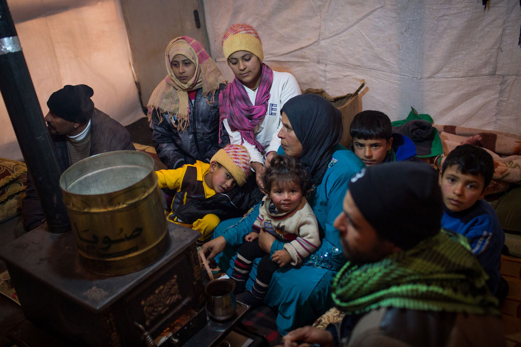 Members of a Syrian refugee family huddle around a stove inside their shelter in Lebanon’s Bekaa Valley. Photo: UNHCR/A. McConnell