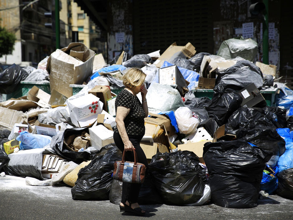 A Lebanese woman holds her nose from the smell as she passes by a pile of garbage on a street in Beirut, Lebanon, Tuesday, July 21, 2015. Garbage is piling up on the streets of Beirut amid a growing dispute over tiny Lebanon's largest trash dump. (AP Photo/Hassan Ammar)
